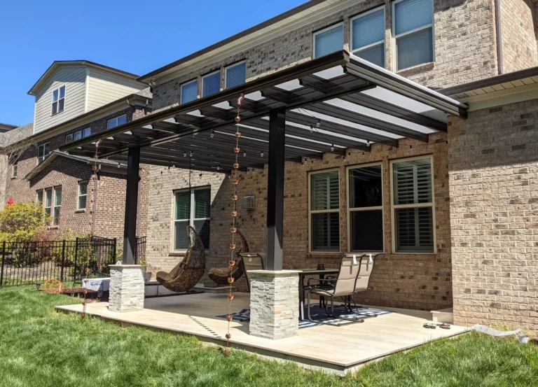 Translucent Patio Roof Panels Let in Light, Shed Rain 2 A patio area with a metal pergola featuring hanging string lights, two swinging chairs, and a dining table with chairs. The backdrop includes a brick house with large windows, and a well-maintained lawn.